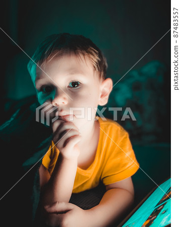 Little boy looking at a tablet in the evening in the dark on the bed Little boy looking at a tablet in the evening in the dark on the bed 87483557