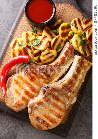 Spicy meat grilled spare Pork Chops and grilled potatoes on a wooden board on the table closeup. Vertical top view 87483596