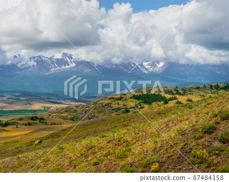 Atmospheric summer mountain landscape. Dramatic landscape with the big mountains in a light fog under white clouds. Altai Mountains. Atmospheric summer mountain landscape. Dramatic landscape with the big mountains in a light fog under white clouds. Altai Mountains. 87484158