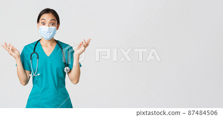 Covid-19, coronavirus disease, healthcare workers concept. Surprised and amazed asian female nurse, physician in medical mask and scrubs raising hands up excited, hear amazing news, white background 87484506
