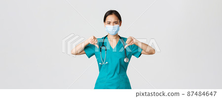 Covid-19, coronavirus disease, healthcare workers concept. Disappointed and upset asian female doctor in scrubs and medical mask showing thumbs-up, disagree or prohibit something, give advice Covid-19, coronavirus disease, healthcare workers concept. Disappointed and upset asian female doctor in scrubs and medical mask showing thumbs-up, disagree or prohibit something, give advice 87484647