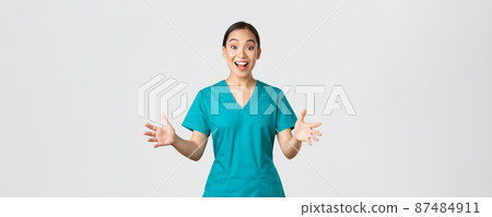 Covid-19, healthcare workers, pandemic concept. Happy and surprised asian nurse in scrubs raising hands excited and smiling. Doctor congratulate with great news, applause, white background 87484911