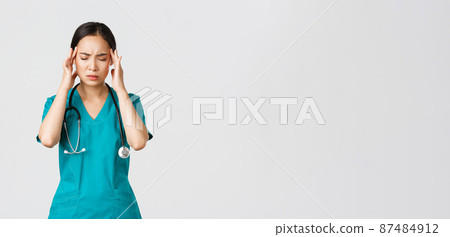Covid-19, healthcare workers, pandemic concept. Overworked and tired young asian female nurse close eyes, grimacing from headache, feel dizzy, night shift with coronavirus patients, white background 87484912