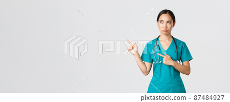 Covid-19, healthcare workers, pandemic concept. Disappointed gloomy, sulking asian nurse in scrubs, female doctor looking displeased, pointing upper left corner and frowning judgemental 87484927