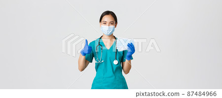 Covid-19, coronavirus disease, healthcare workers concept. Smiling asian doctor, nurse in scrubs and rubber gloves, showing thumbs-up and medical masks, white background 87484966