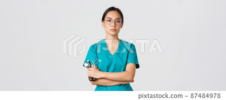 Covid-19, coronavirus disease, healthcare workers concept. Professional confident, serious-looking female doctor, physician in glasses and scrubs, holding stethoscope, standing white background 87484978