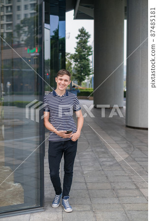 Portrait of young caucasian man in casual clothes standing outdoors and holding his phone. High quality photo 87485181