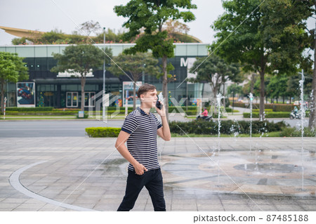 Portrait of young caucasian man in casual clothes walking outdoors and making phone call. Using smartphone, talking by the phone. Urban lifestyle. Portrait of young caucasian man in casual clothes walking outdoors and making phone call. Using smartphone, talking by the phone. Urban lifestyle. 87485188