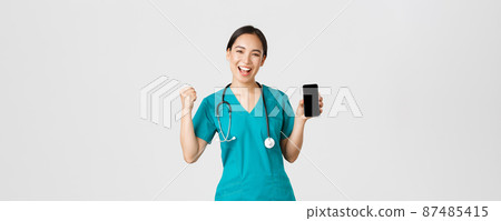 Covid-19, healthcare workers and online medicine concept. Successful cheerful asian female doctor, nurse in scrubs fist pump in rejoice, showing smartphone screen app and looking pleased at camera Covid-19, healthcare workers and online medicine concept. Successful cheerful asian female doctor, nurse in scrubs fist pump in rejoice, showing smartphone screen app and looking pleased at camera 87485415