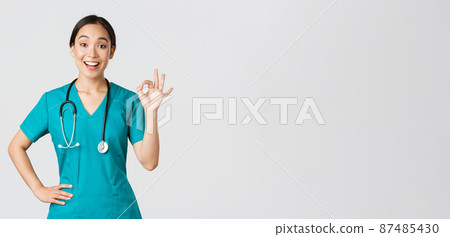 Covid-19, healthcare workers, pandemic concept. Surprised and happy asian female doctor, nurse in scrubs showing okay gesture and smiling amazed, praise nice work, agree with someone 87485430