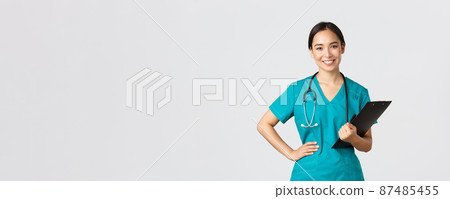 Healthcare workers, preventing virus, quarantine campaign concept. Smiling pleasant asian female physician, doctor during examination wearing scrubs and holding clipboard, white background 87485455