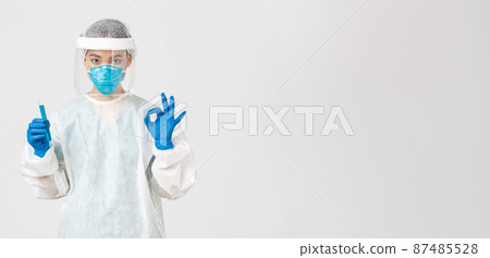 Covid-19, coronavirus disease, healthcare workers concept. Serious asian female doctor, professional researcher in personal protective equipment showing okay gesture, holding test-tube with vaccine 87485528