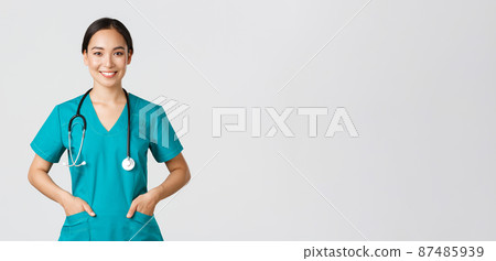 Covid-19, healthcare workers, pandemic concept. Confident smiling pretty asian female doctor, physician looking determined and upbeat, holding hands in pockets of scrubs, examine patients in clinic Covid-19, healthcare workers, pandemic concept. Confident smiling pretty asian female doctor, physician looking determined and upbeat, holding hands in pockets of scrubs, examine patients in clinic 87485939