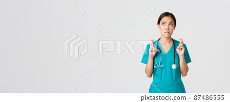 Covid-19, healthcare workers, pandemic concept. Hopeful nervous asian female intern in scrubs waiting for news, doctor cross fingers and biting lip as looking upper left corner, praying 87486555