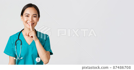Healthcare workers, preventing virus, quarantine campaign concept. Smiling pretty asian doctor, nurse in scrubs smiling, shushing, asking stay quiet, standing white background Healthcare workers, preventing virus, quarantine campaign concept. Smiling pretty asian doctor, nurse in scrubs smiling, shushing, asking stay quiet, standing white background 87486708