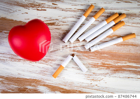 Quit smoking. Rubber heart and cigarettes on a wooden background. Cardiovascular health 87486744