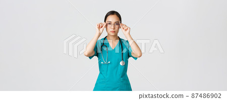Covid-19, healthcare workers, pandemic concept. Confident serious-looking and determined asian female doctor, nurse in scrubs put on glasses, ready for shift in emergency room, white background 87486902