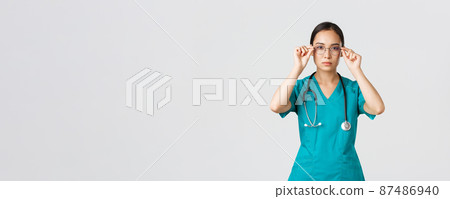 Covid-19, healthcare workers, pandemic concept. Confident serious-looking and determined asian female doctor, nurse in scrubs put on glasses, ready for shift in emergency room, white background 87486940