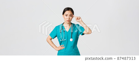 Covid-19, healthcare workers, pandemic concept. Annoyed skeptical asian female nurse or doctor scolding someone acting crazy or stupid, roll finger over temple with judgemental face 87487313