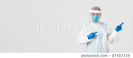 Covid-19, coronavirus disease, healthcare workers concept. Surprised and intrigued asian female doctor, tech lab employee in personal protective equipment look amazed and pointing fingers right 87487339