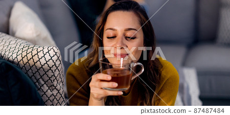 Young pretty woman drinks a cup of tea while lying on the couch 87487484