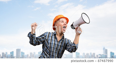 Expressive woman in helmet shouting into megaphone 87487990