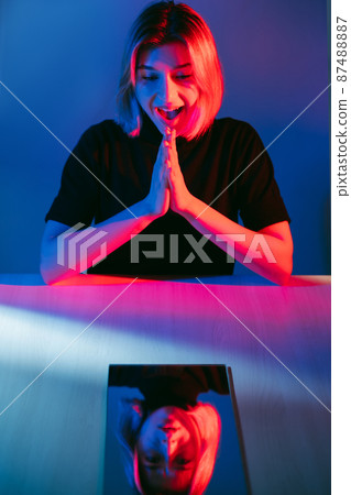 Bipolar disorder. Color light portrait. Emotional conflict. Excited woman with upset depressed face mirror reflection in pink blue neon glow isolated on dark. Bipolar disorder. Color light portrait. Emotional conflict. Excited woman with upset depressed face mirror reflection in pink blue neon glow isolated on dark. 87488887