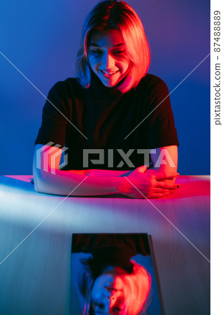 Emotional crisis. Color light portrait. Dual personality. Enthusiastic smiling girl with upset depressed tired face mirror reflection in pink blue neon light isolated on dark. Emotional crisis. Color light portrait. Dual personality. Enthusiastic smiling girl with upset depressed tired face mirror reflection in pink blue neon light isolated on dark. 87488889