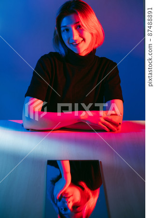 Double face. Neon light portrait. Pretending nice. Curious smiling girl with bored indifferent face mirror reflection in pink blue color glow isolated on dark. Double face. Neon light portrait. Pretending nice. Curious smiling girl with bored indifferent face mirror reflection in pink blue color glow isolated on dark. 87488891