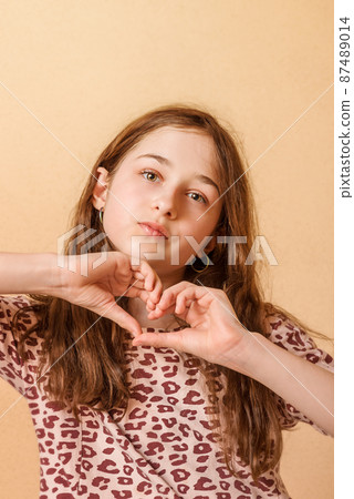 Portrait of a child. Teenage girl shows a heart on a beige background. 87489014