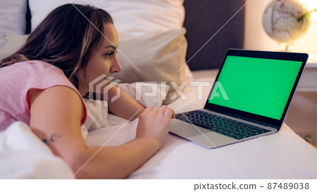 Young woman lies on the bed with her laptop - green screen display 87489038