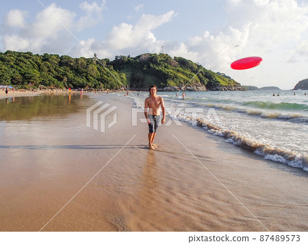 Man is playing with frisbee on Nai Harn beach on Phuket island. Leisure activity outdoors. Thailand. Man is playing with frisbee on Nai Harn beach on Phuket island. Leisure activity outdoors. Thailand. 87489573