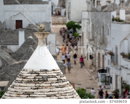 Alberobello,Puglia,Italy. August 2021. Amazing aerial footage of the enchanting historic village. From above, the unmistakable city landscape characterized by conical stone roofs. People in the alleys Alberobello,Puglia,Italy. August 2021. Amazing aerial footage of the enchanting historic village. From above, the unmistakable city landscape characterized by conical stone roofs. People in the alleys 87489659