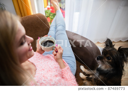The girl sits with a cup of coffee and the pie looks on with interest. The girl sits with a cup of coffee and the pie looks on with interest. 87489773