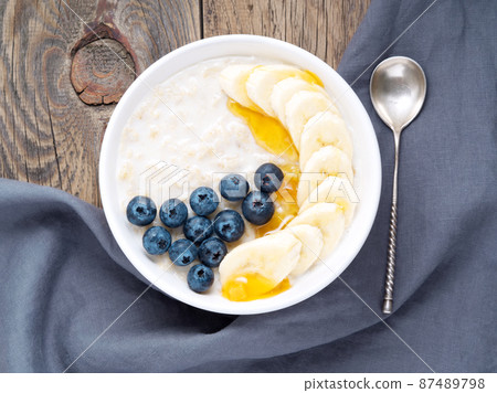 Oatmeal with bananas, blueberries, chia seeds, jam, honey on old rustic wooden background. Healthy breakfast. Top view. 87489798