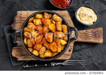 Patatas bravas, spicy potatoes, a Spanish dish with fried potato and a spicy garlic sauce. Black background. Top view 87489865