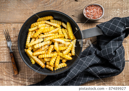 Deep fried Crinkle French fries potatoes sticks in a pan. Wooden background. Top view 87489927