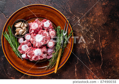 Fresh uncooked beef Oxtail cut Meat on rustic plate with herbs. Dark background. Top view. Copy space Fresh uncooked beef Oxtail cut Meat on rustic plate with herbs. Dark background. Top view. Copy space 87490038