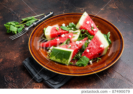 Vegetarian watermelon salad with feta cheese, arugula, onions. Dark background. Top view Vegetarian watermelon salad with feta cheese, arugula, onions. Dark background. Top view 87490079