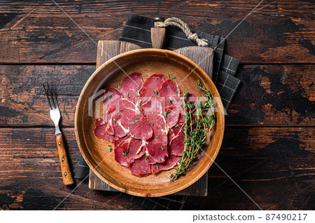 Pastrami slices, dried beef meat with herbs in wooden plate. Wooden background. Top view Pastrami slices, dried beef meat with herbs in wooden plate. Wooden background. Top view 87490217