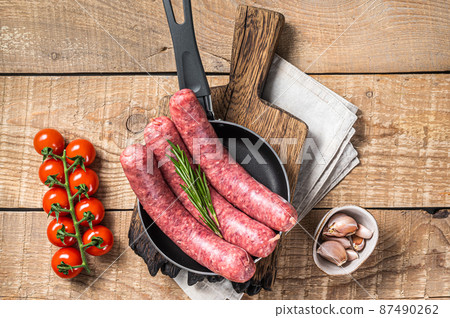 Raw sausages ready for cooking in a skillet, uncooked meat. Wooden background. Top view 87490262