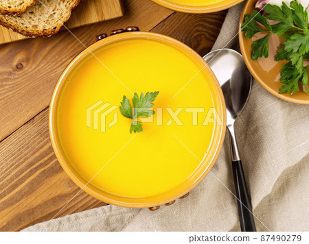 brown bowl of pumpkin soup with parsley on brown dark wooden background, top view, close up brown bowl of pumpkin soup with parsley on brown dark wooden background, top view, close up 87490279