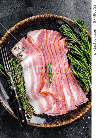 Raw sliced bacon ready for cooking with herbs. Black background. Top view 87490552