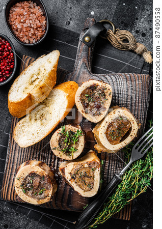 Roast marrow calf bones on wooden board with bread and herbs. Black background. Top view Roast marrow calf bones on wooden board with bread and herbs. Black background. Top view 87490558