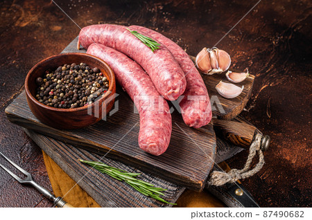 Bratwurst Raw meat sausages on wooden board with spices. Dark background. Top view 87490682