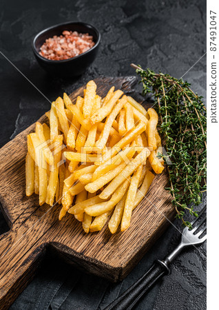 Tasty french fries on wooden cutting board. Black background. Top view Tasty french fries on wooden cutting board. Black background. Top view 87491047