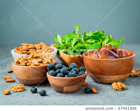 Healthy vegan food - dry fruits, greens, nuts, berry. Superfoods on gray stone background, side view. Healthy vegan food - dry fruits, greens, nuts, berry. Superfoods on gray stone background, side view. 87491806