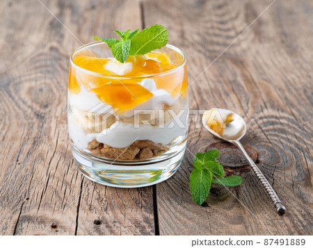 Healthy layered dessert with yogurt, banana, mango jam, cookie on wooden background, side view 87491889