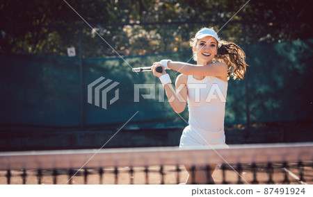 Woman forcefully playing tennis in court Woman forcefully playing tennis in court 87491924