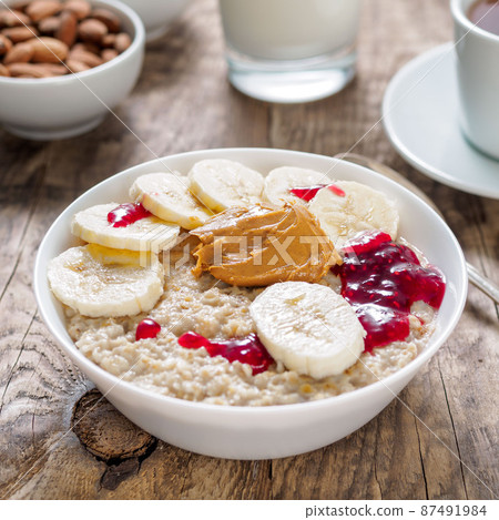 Healthy Breakfast in the morning - oatmeal with slices of bananas, raspberry jam and peanut butter. Side view. 87491984